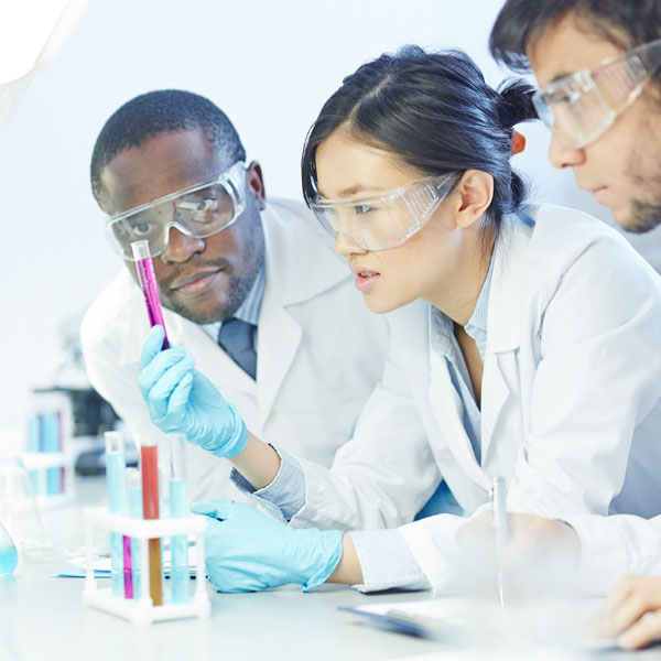 Goggled research scientists examine test tubes full of colored liquids.